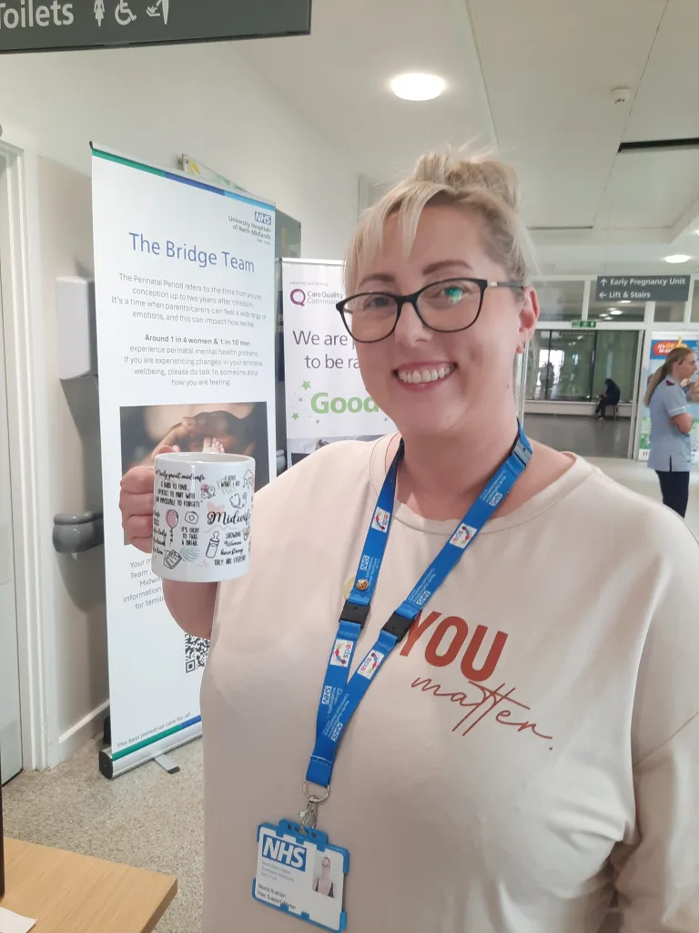 Nic Rushton, a Combined Healthcare peer support worker, posing with a mug and smiling
